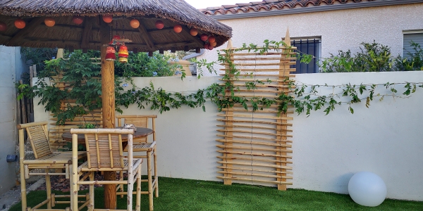 Panneaux décoratifs en ganivelles et piquets en bois fixés sur un mur blanc, dans un jardin